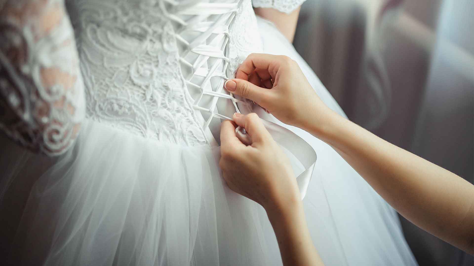 A woman is putting a button on a wedding dress.