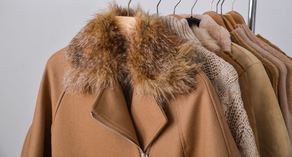 A row of winter coats with fur collars hanging on a rack.