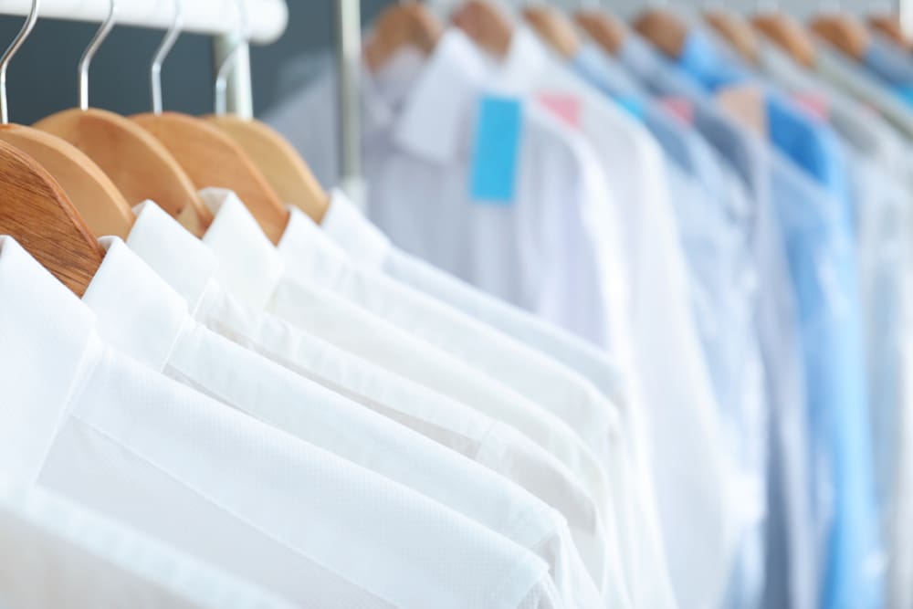 Row of medical lab coats and scrubs hanging on a rack, with focus on white coats in the foreground and blue scrubs in the background.