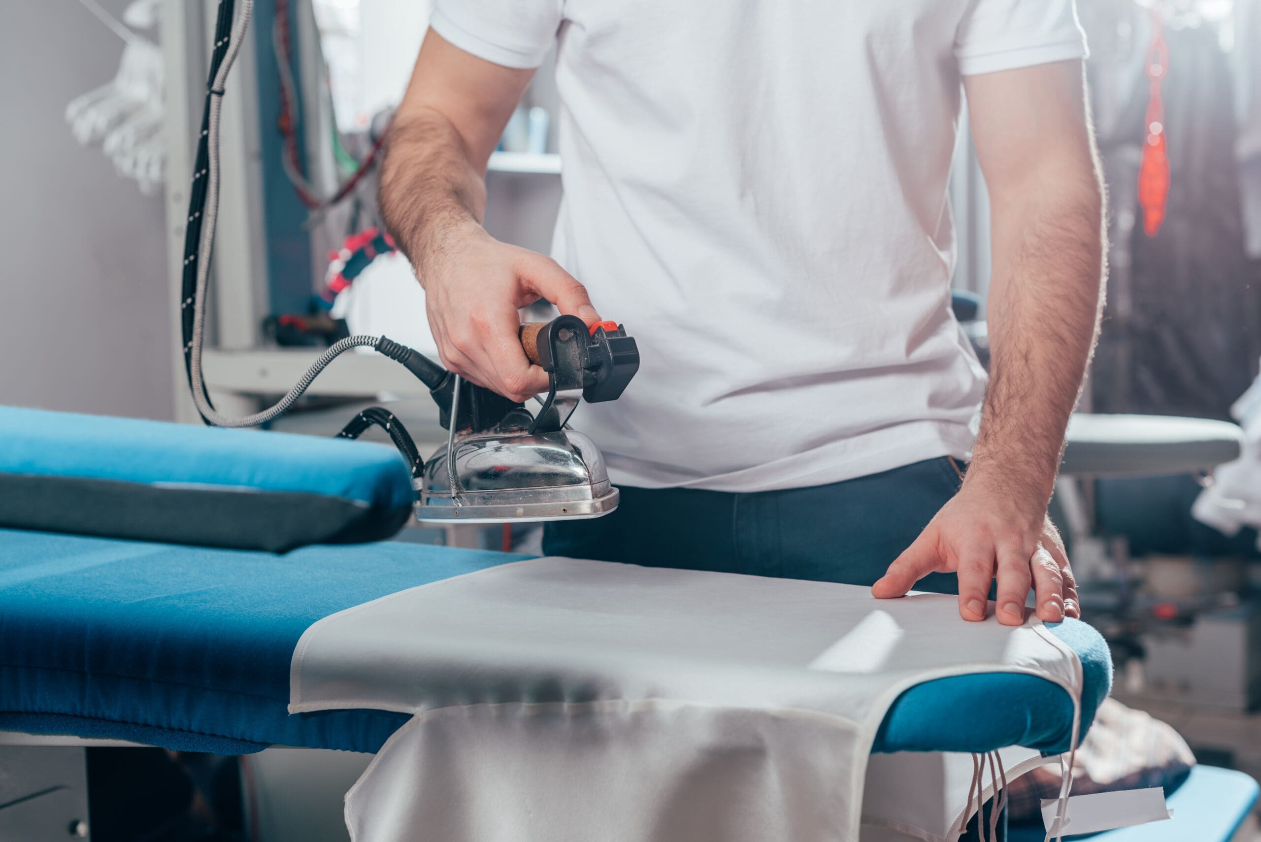 Person ironing clothes using a professional steam iron at a laundry service.