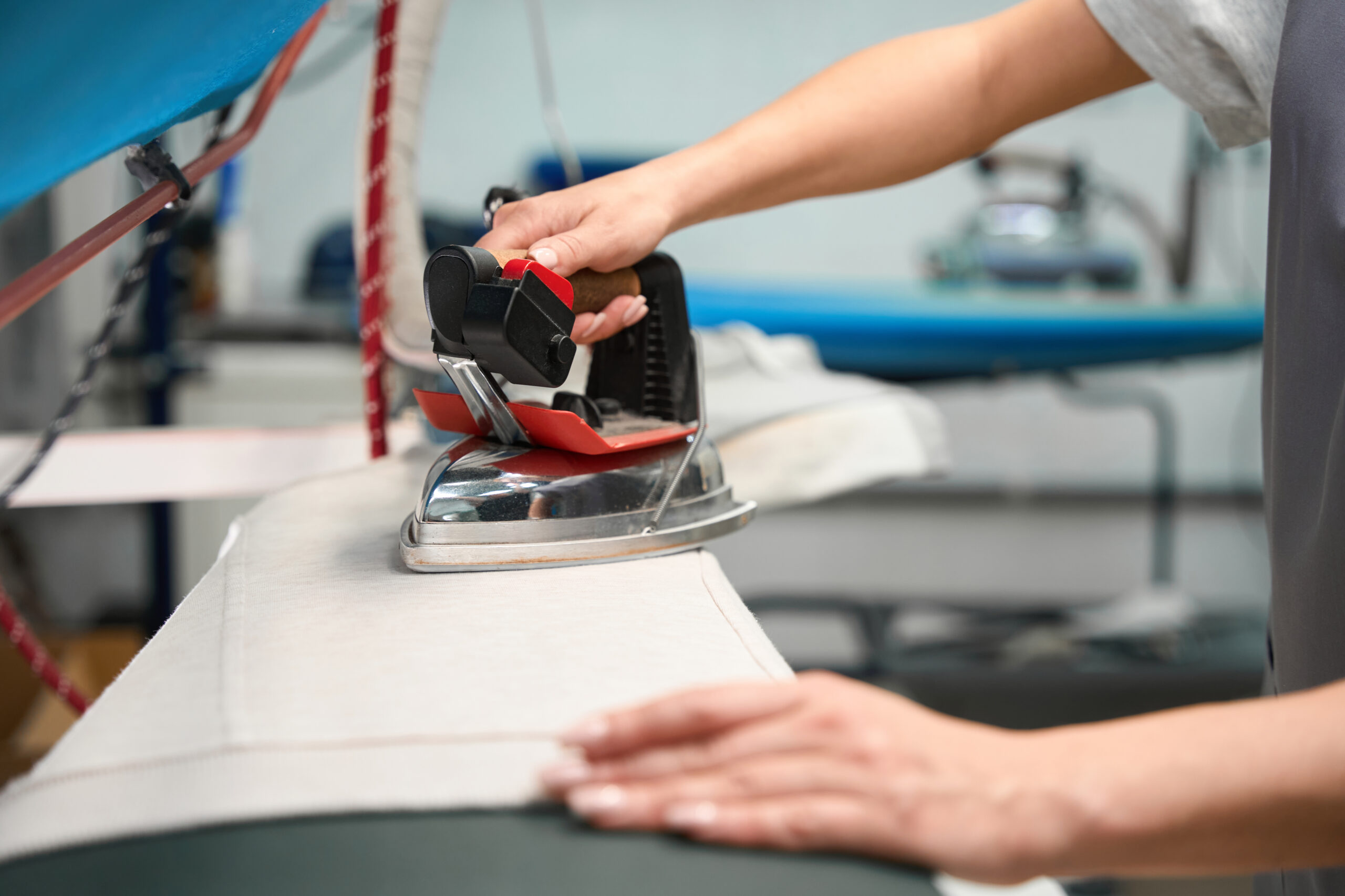 A person's hands using a professional iron on fabric over an ironing board in a tailoring workshop.