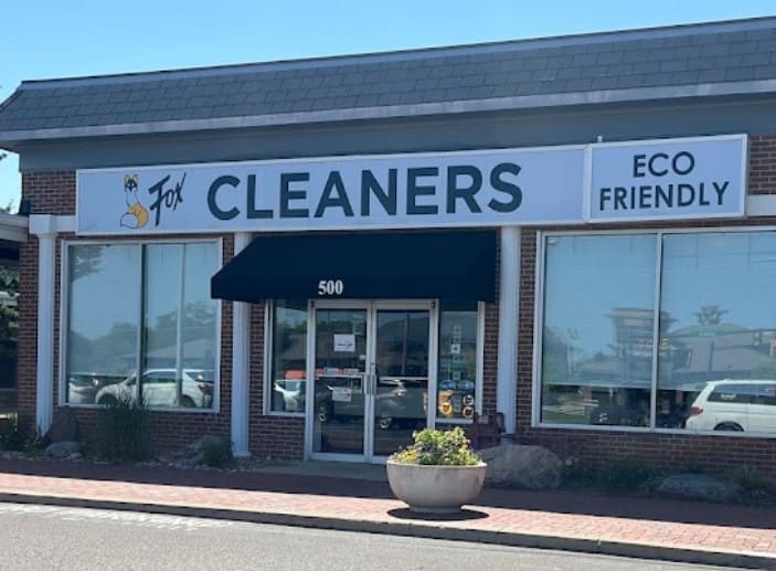A storefront of Fox Cleaners with a sign indicating "Eco Friendly." The entrance has a black awning and the store address is 500. There is a large glass window and a planter outside.
