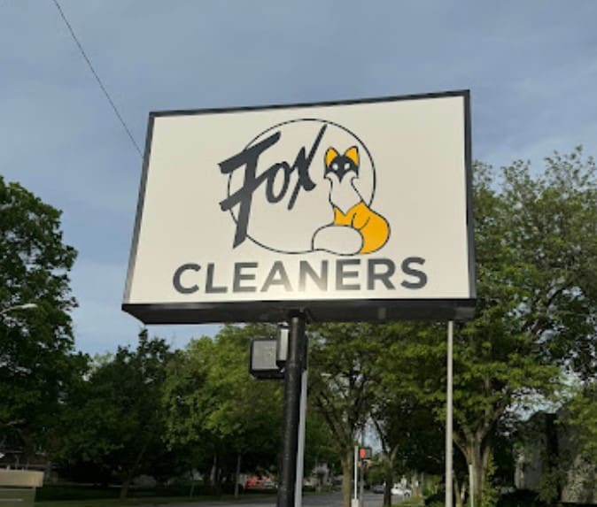 Signage for "Fox Cleaners" featuring the brand name and a fox graphic, set against trees and a partly cloudy sky.