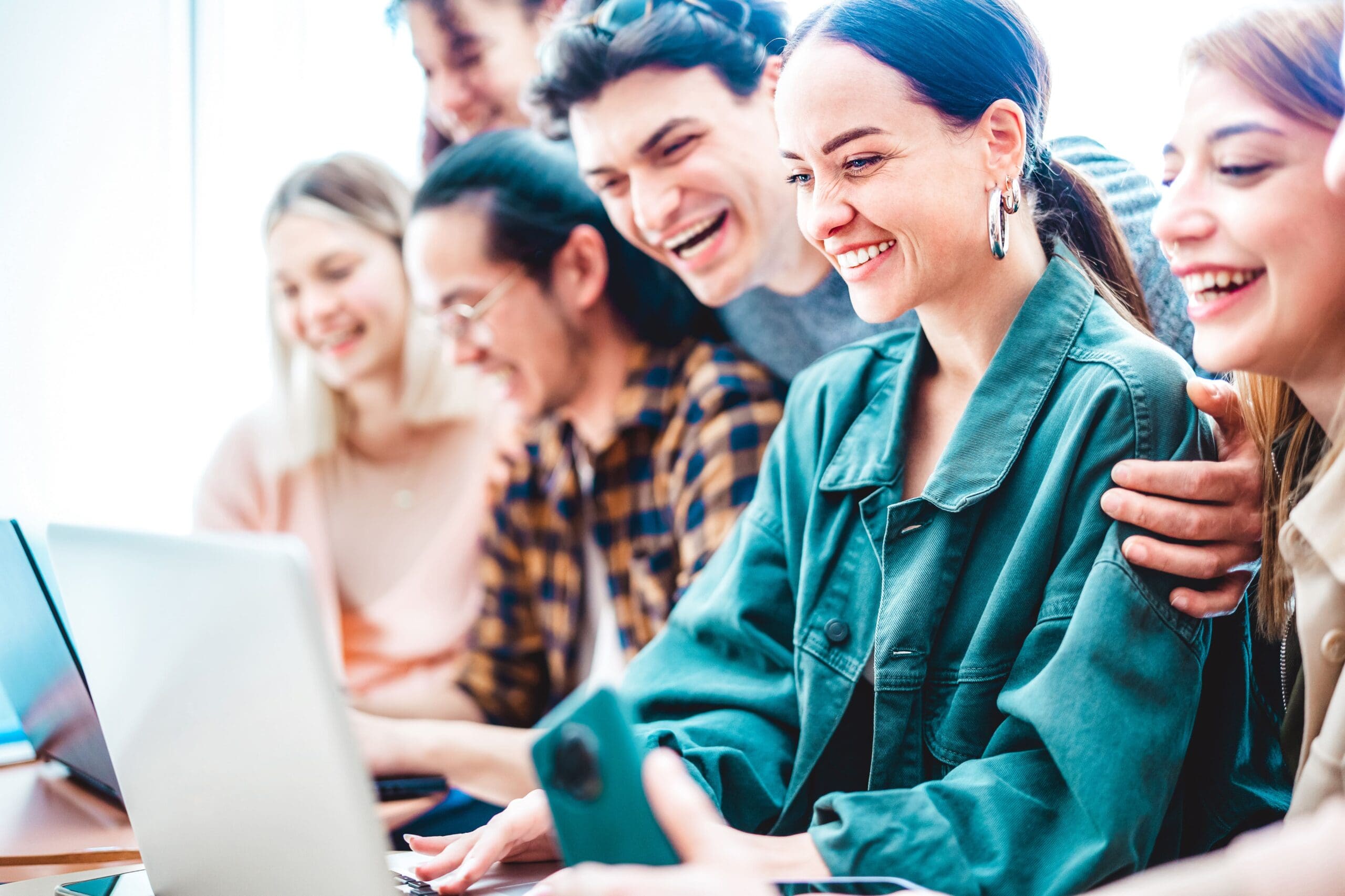 A group of people smiling and looking at a laptop screen together, appearing engaged and happy.