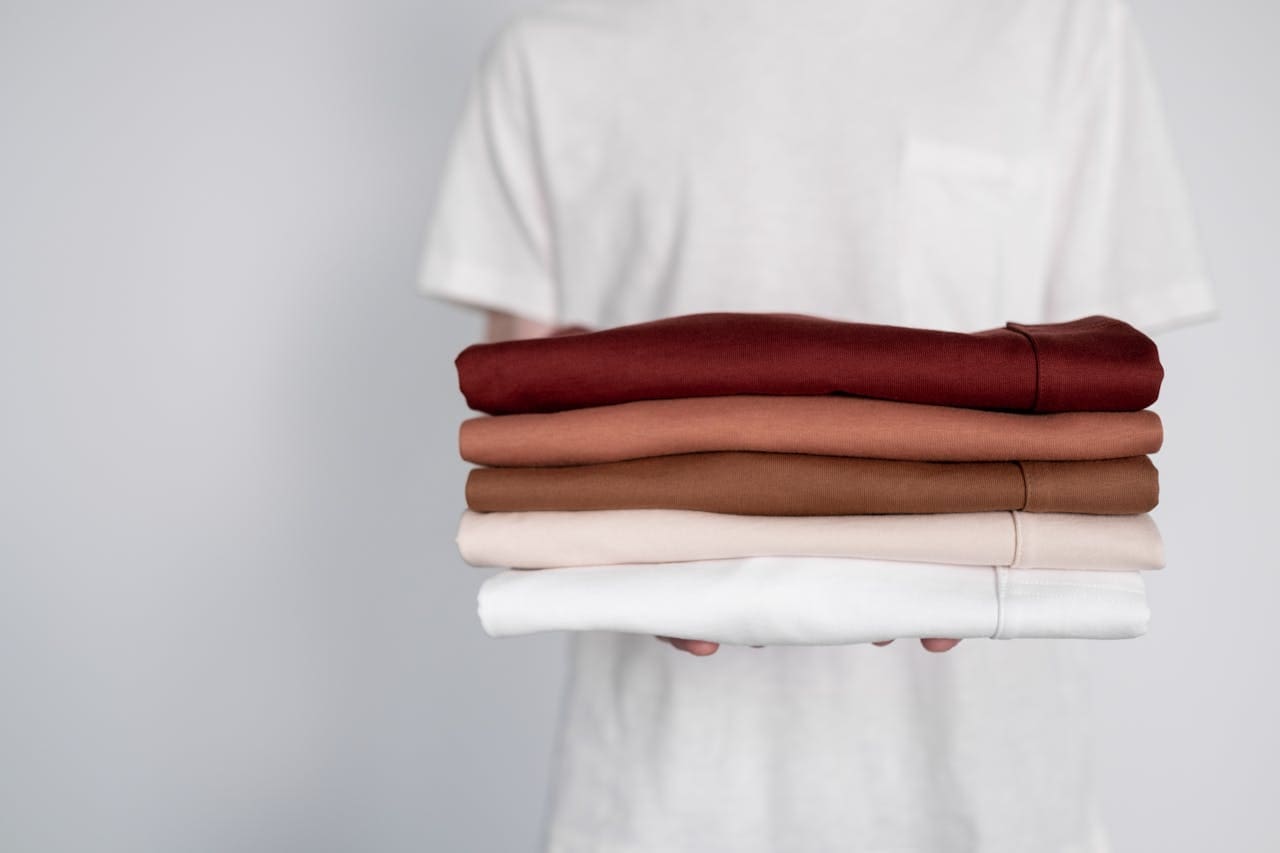 Person in a white shirt holding a stack of neatly folded clothes in various shades of red, brown, and white at a Dry Cleaning and Laundry Service in Dayton.