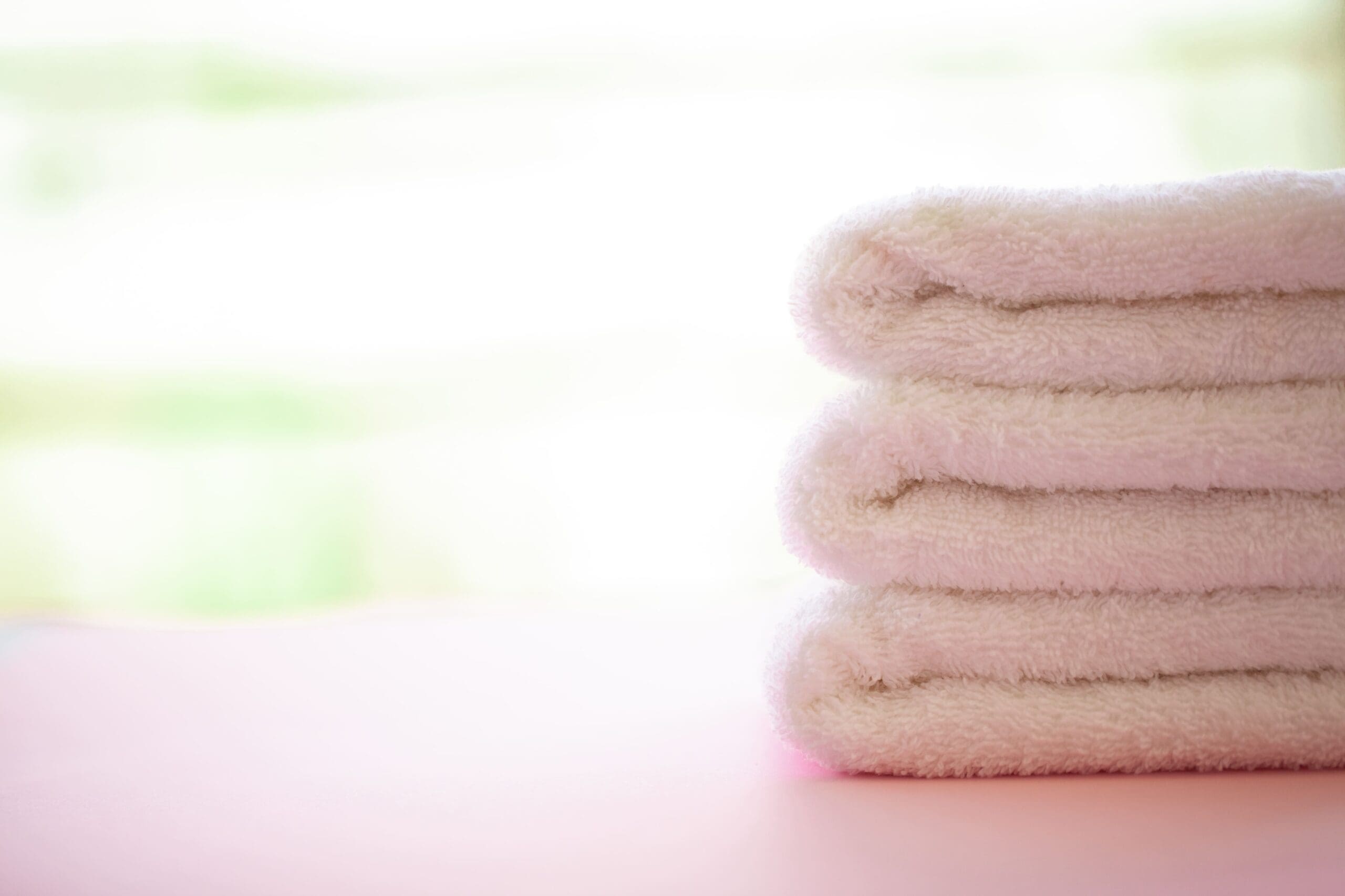 A stack of four neatly folded white towels on a light surface with a blurred background.