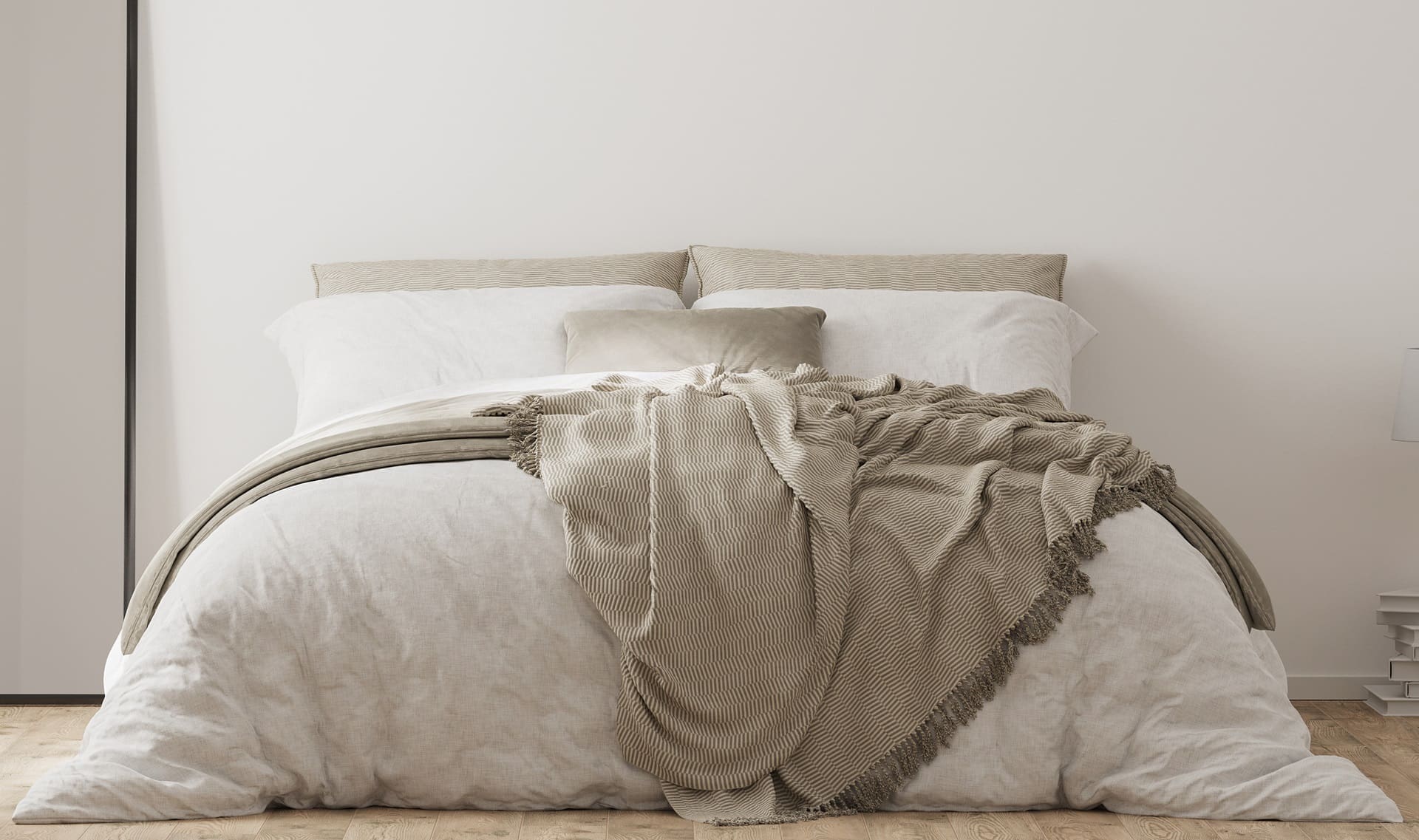 A neatly made bed with white and beige bedding, featuring a beige textured throw draped over the end. Neutral pillows are arranged at the head of the bed against a plain white wall.