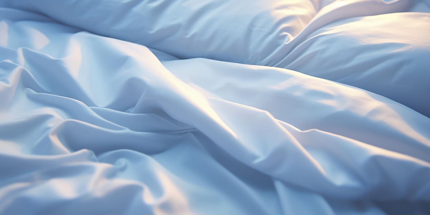 Wrinkled white bedsheets with soft lighting and shadows.