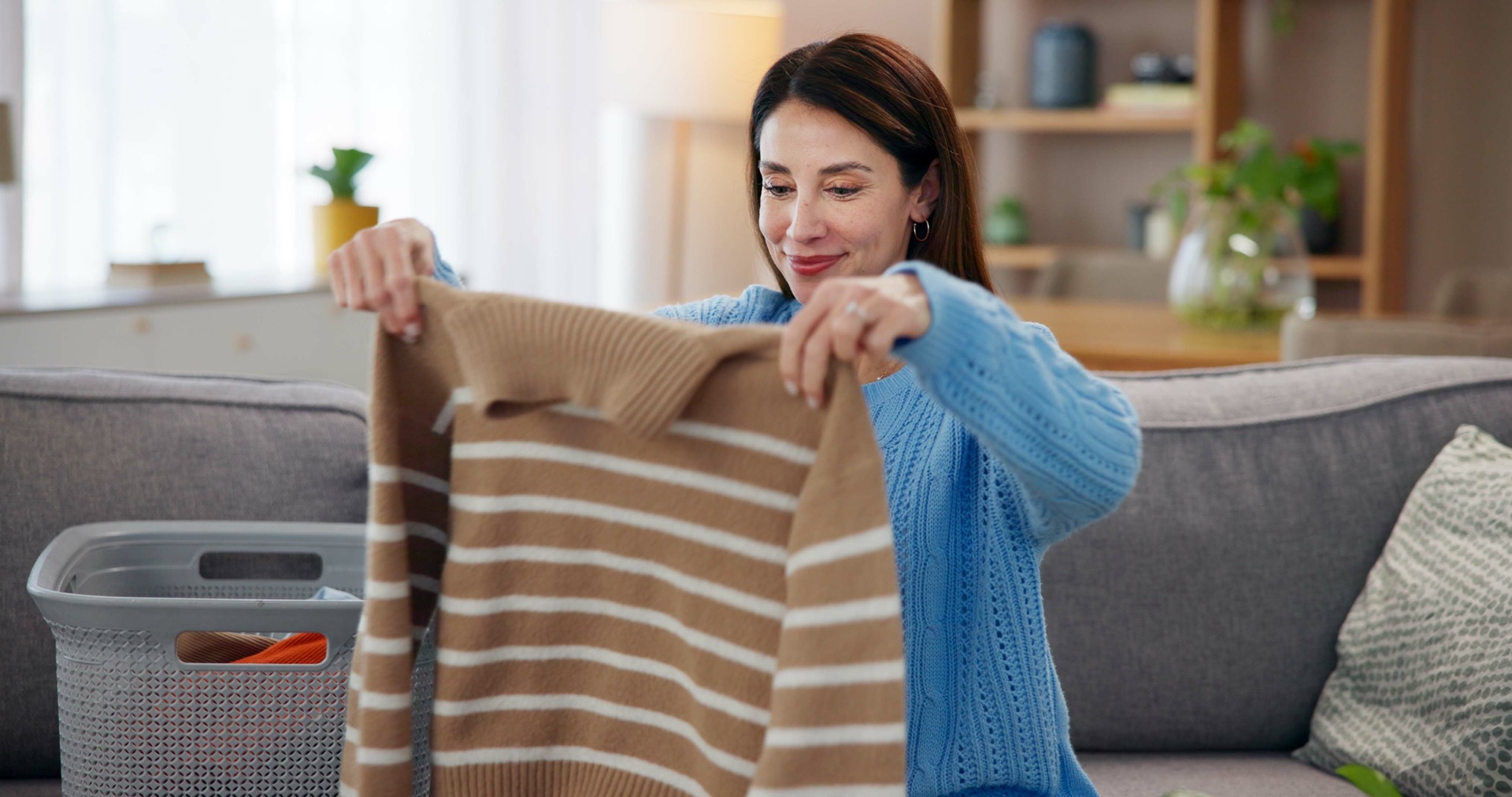 Woman holding a brown and white striped sweater, sitting on a sofa in a cozy living room.